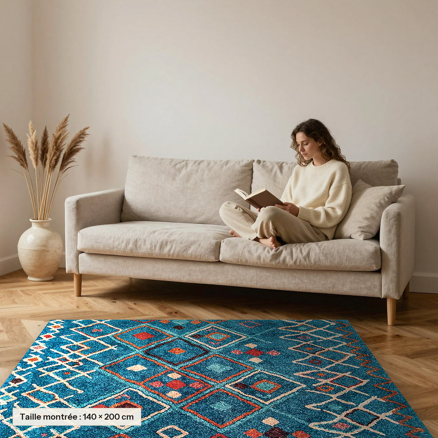 Tapis berbère coloré Tawsimt, bleu canard à médaillons posé devant un canapé, taille 140 × 200 cm