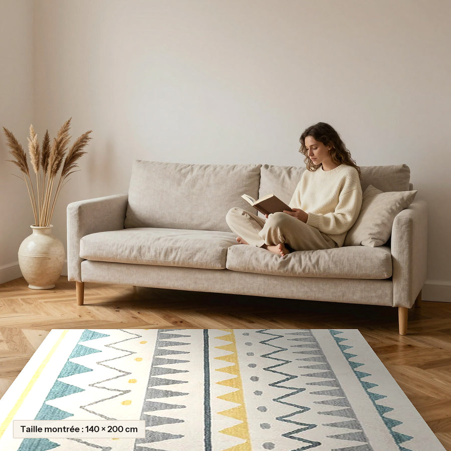 Tapis berbère coloré Tafila, triangles gris et safran posé devant un canapé, taille 140 × 200 cm