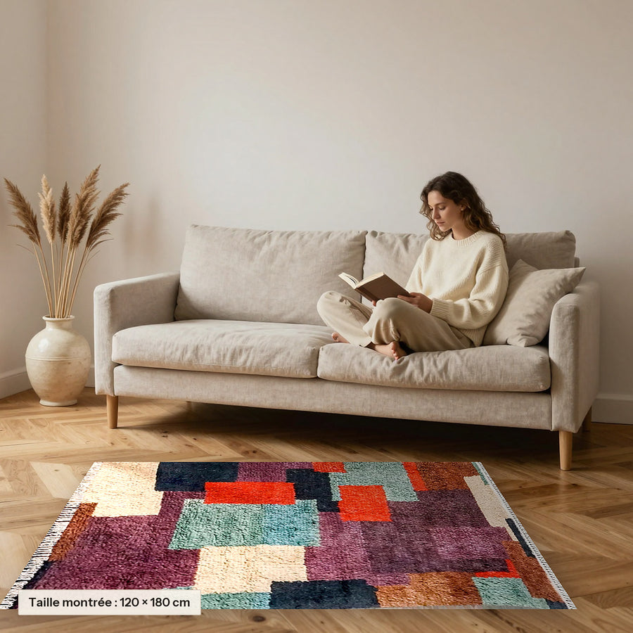 Tapis berbère coloré Tafsut, patchwork prune et orange posé devant un canapé, taille 120 × 180 cm