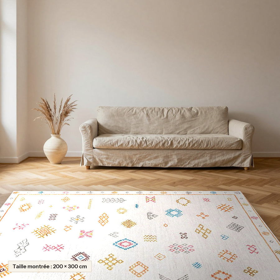 Tapis berbère coloré Tamallat, écru à symboles colorés posé dans un salon, taille 200 × 300 cm