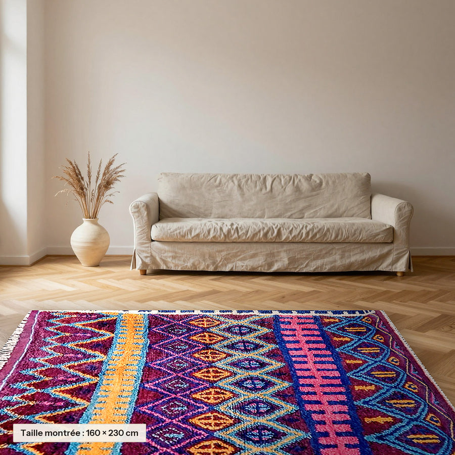Tapis berbère coloré Thiyya, violet et rose posé dans un salon, taille 160 × 230 cm