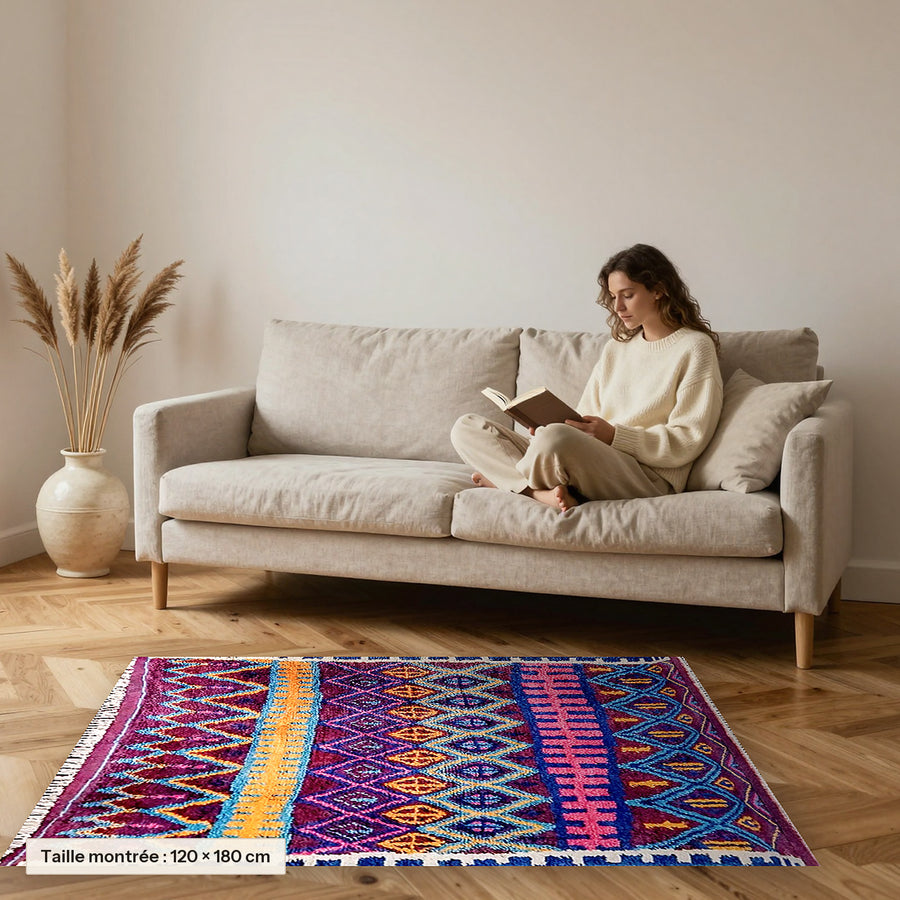 Tapis berbère coloré Thiyya, violet et rose posé devant un canapé, taille 120 × 180 cm
