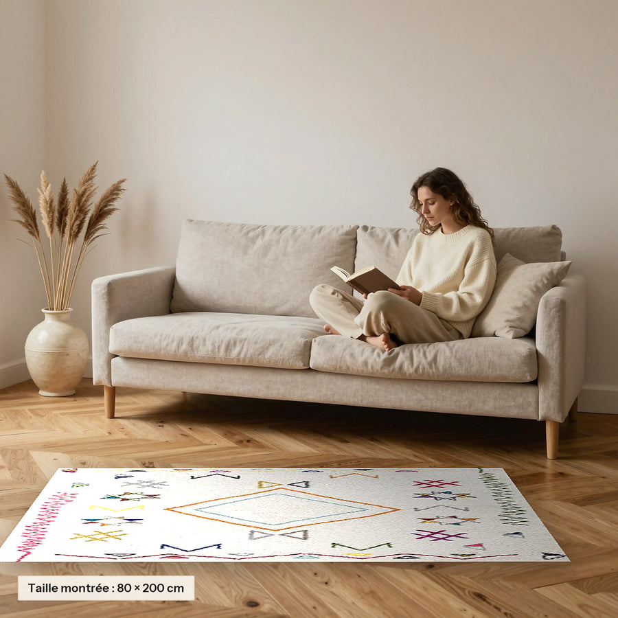 Tapis berbère coloré Yani, écru à symboles tribaux posé devant un canapé, taille 80 × 200 cm