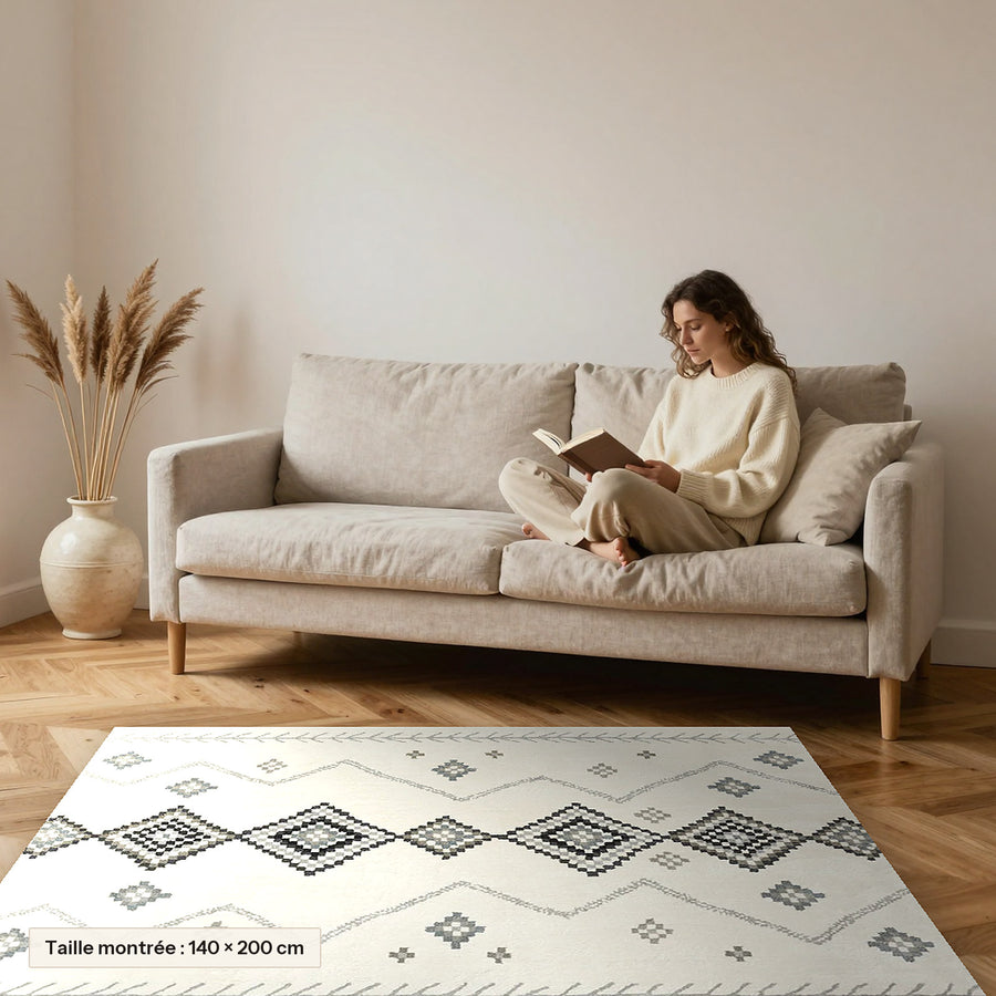 Tapis Beni Ouarain Taysa, écru à losanges gris posé devant un canapé, taille 140 × 200 cm